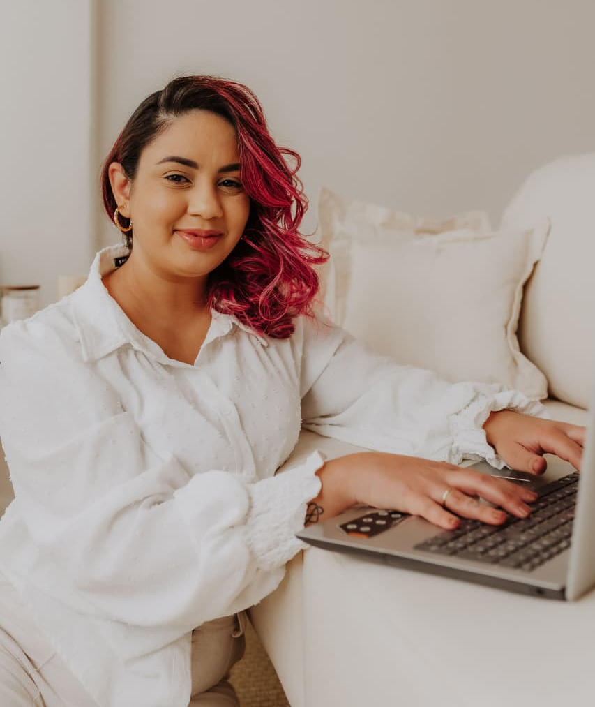 Psicóloga Jéssica de Mattos sorrindo enquanto utiliza um notebook para realizar atendimento de psicoterapia online, em um ambiente acolhedor e profissional.