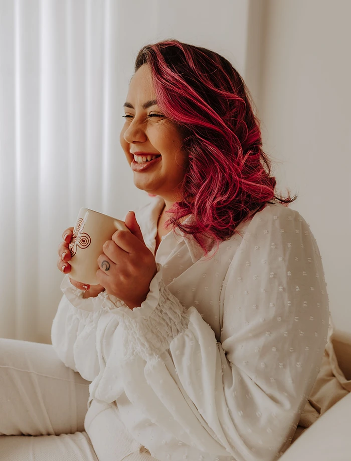 Psicóloga Jéssica Mattos em um momento de acolhimento e humanidade, sorrindo e segurando uma caneca de chá para ilustrar a sensibilidade da sua prática clínica em Terapia ACT.